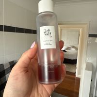 A hand holding a clear bottle of Korean ginseng essence water skincare product in a bathroom setting