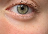 Close-up photograph of a human eye with green-hazel iris and natural eyelashes