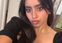 A person taking a selfie indoors with long dark hair wearing a black top