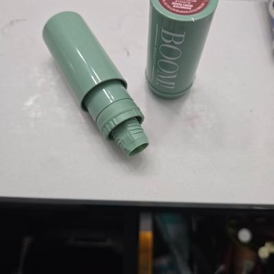 Green cosmetic stick product with cap removed showing twist-up mechanism, lying on white surface