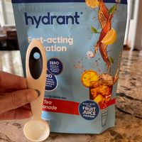A package of Hydrant fast-acting hydration drink mix in iced tea lemonade flavor being held next to a white measuring spoon on a granite countertop