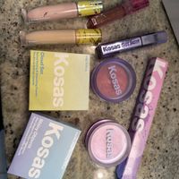 Various Kosas cosmetic products including concealers, blush compacts, lip gloss, and skincare items arranged on a granite countertop