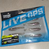 Package of fishing lures on a white surface with fishing equipment in the background